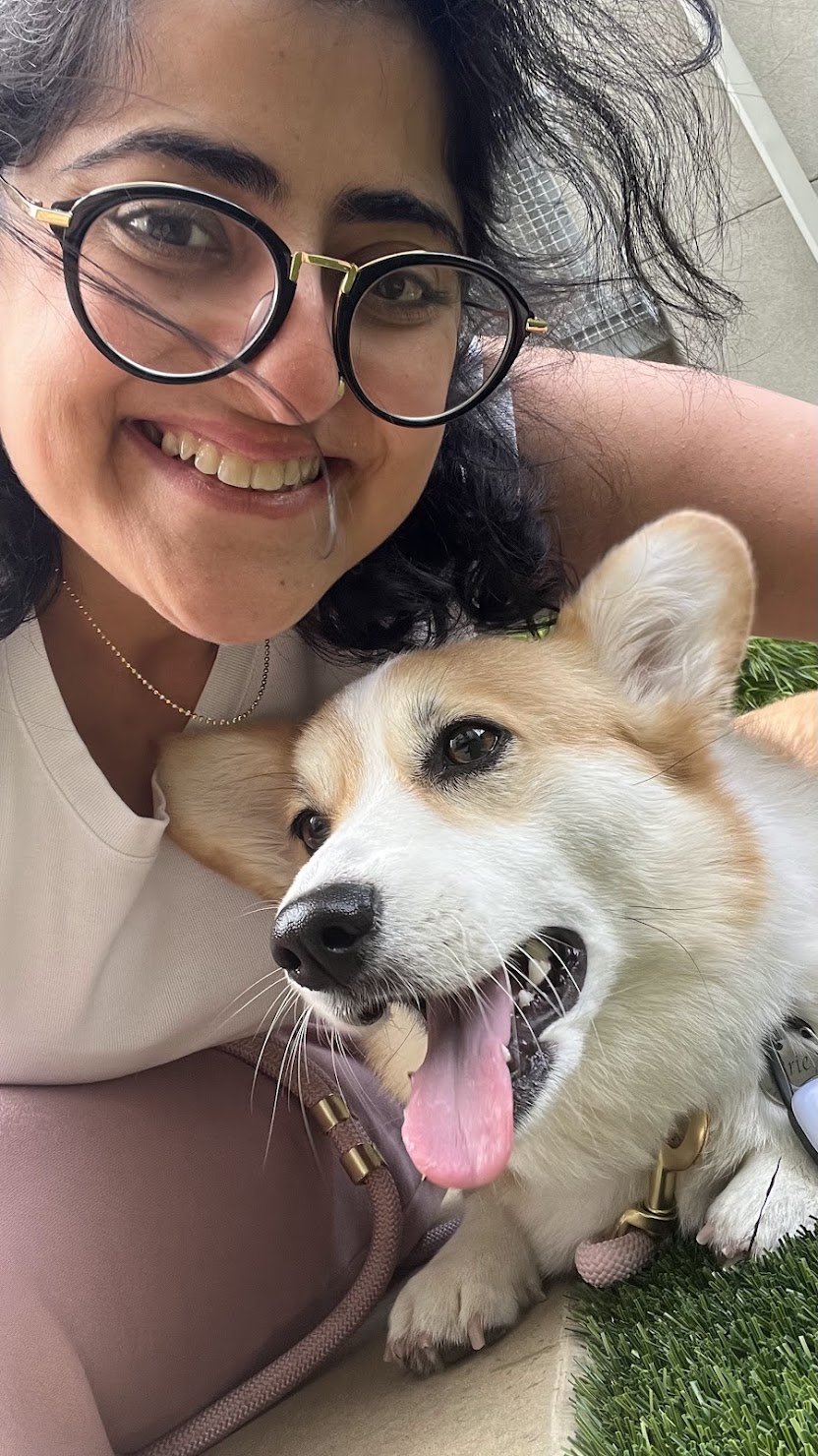 Ghazal smiling with a corgi resting its head on her shoulder